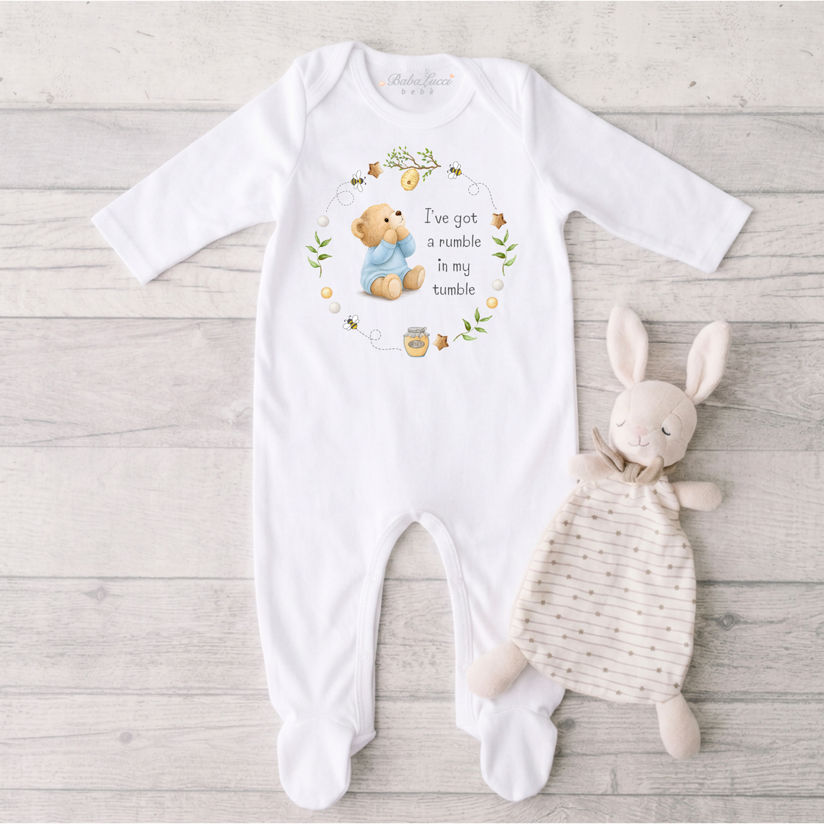 A white long-sleeve baby footed sleepsuit, featuring a teddy bear graphic and the text 'I've got a rumble in my tumble.' 